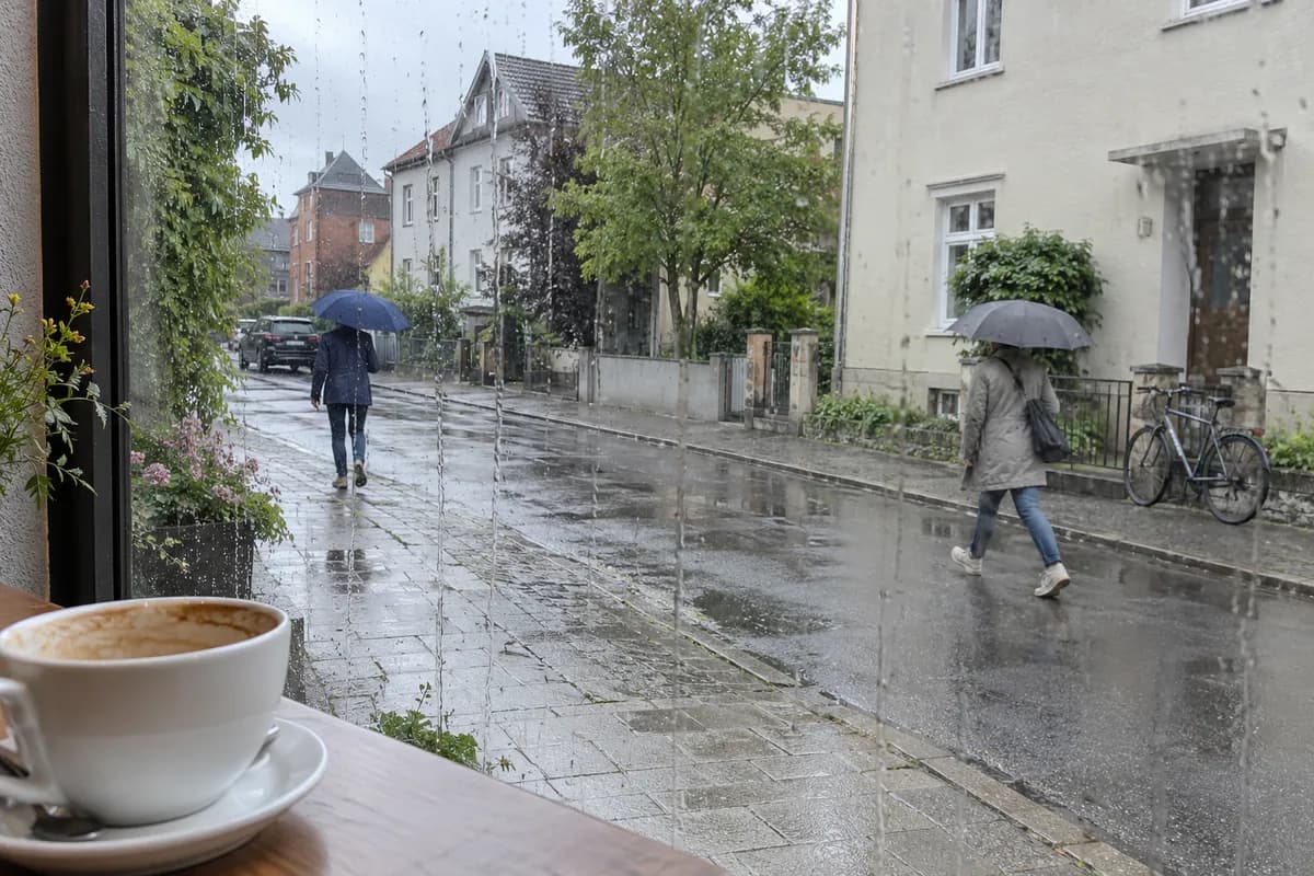 AI-created illustrative scene: People with umbrellas on a rainy street, viewed from a cafe.