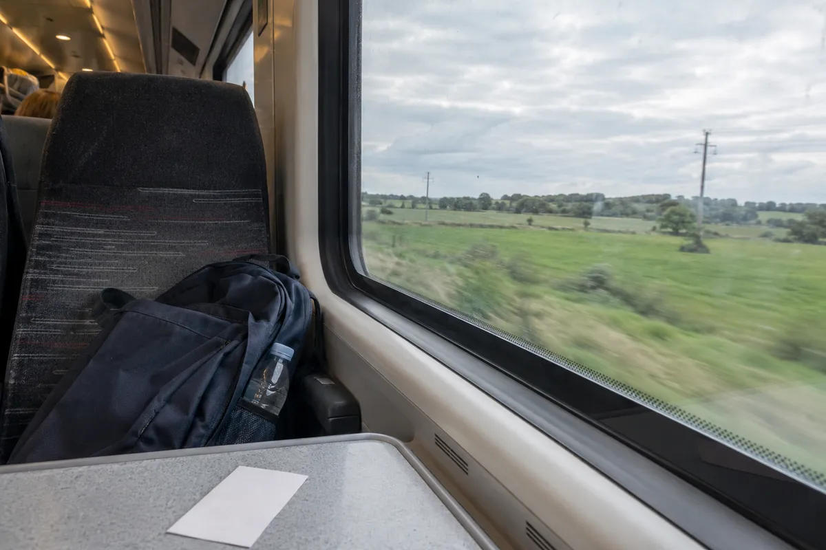AI-created illustrative scene: A backpack on an ordinary train seat beside a countryside window.